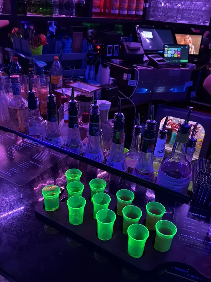 Ein Tablett mit zwölf grün leuchtenden Shots an der Bar, dahinter Flaschen mit Ausgießern