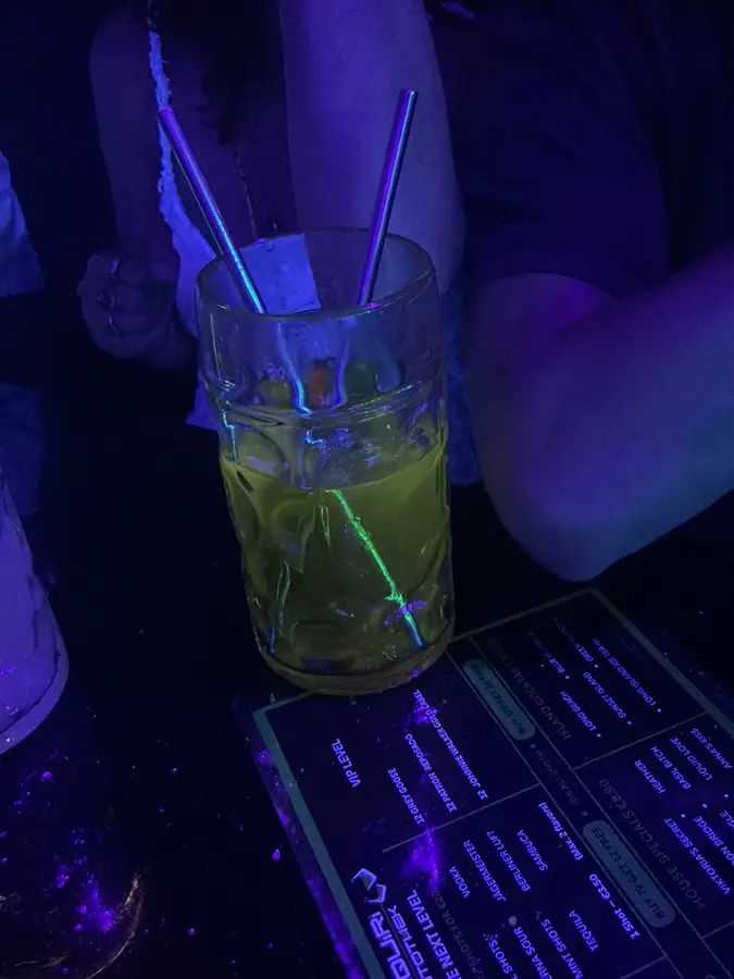Ein Longdrink mit Metallstrohhalmen im Schwarzlicht, daneben die Karte der Shotothek